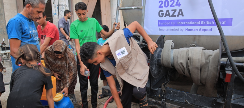 Best Sadaqah Jariyah For Deceased A group of people, including children and adults, gather around a water truck during a humanitarian water distribution in Gaza. A volunteer wearing a vest labeled "International British Waqf" is filling jerry cans from the truck. The sign on the truck reads "Water Project 2024 Gaza," funded by International British Waqf and implemented by Human Appeal.