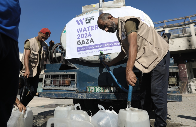 How to make a charitable waqf Aid workers distribute water from a tanker in Gaza, filling plastic containers. A banner reads "Water 2024 Gaza," indicating humanitarian support.