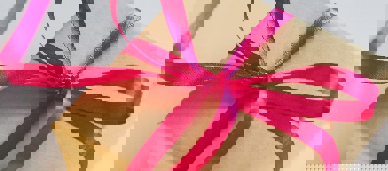 Gift wrapped in brown paper with a bright pink ribbon tied in a bow.